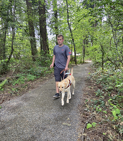 Ethan Edwards and his guide dog, Ginsburg, walk along a wooded path.